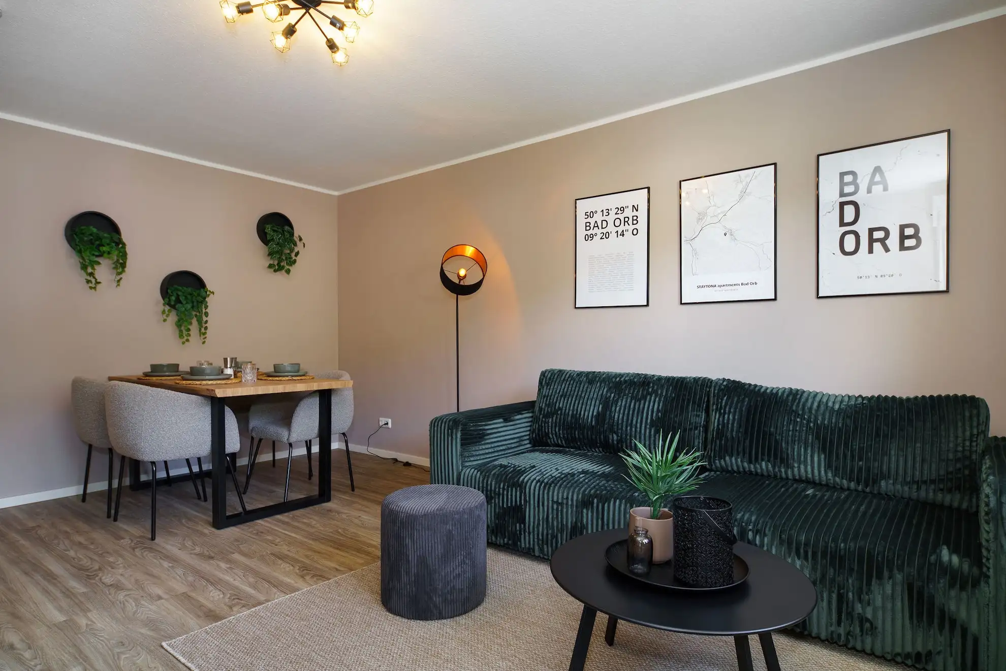 Wohnbereich mit dunkelgrünem Sofa, rundem Couchtisch, gedecktem Holzesstisch und vier grauen Polsterstühlen.